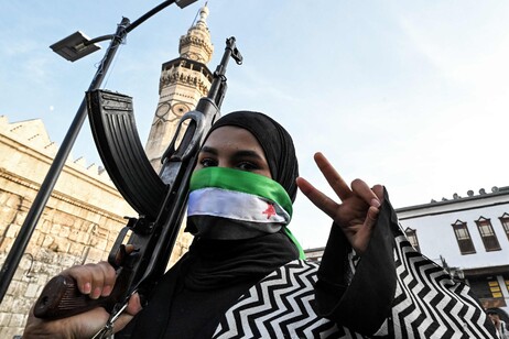 Mulher mascarada celebra queda de Assad diante de mesquita em Damasco, capital da Síria