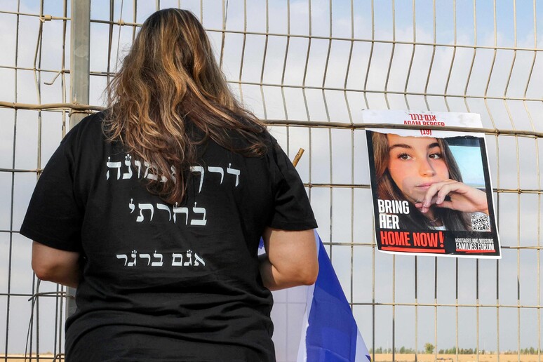 Mulher diante de cartaz com rosto da refém Agam Berger na fronteira entre Israel e Gaza © ANSA/AFP